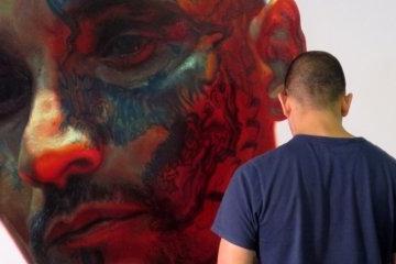 photo of a person with their back to the camera and the painted face of a person in the background